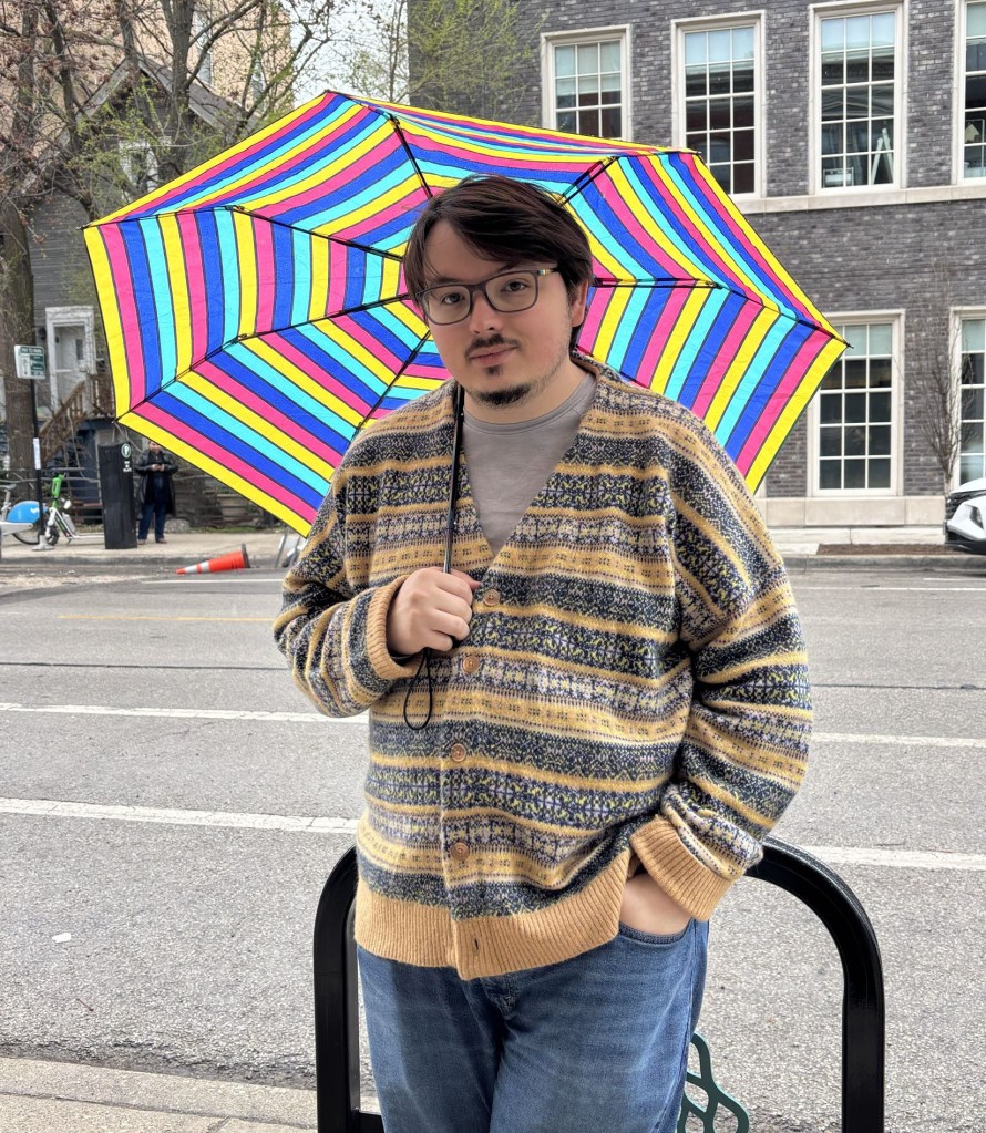 Picture of Rowan Blair in a sweater, jeans, and holding an umbrella